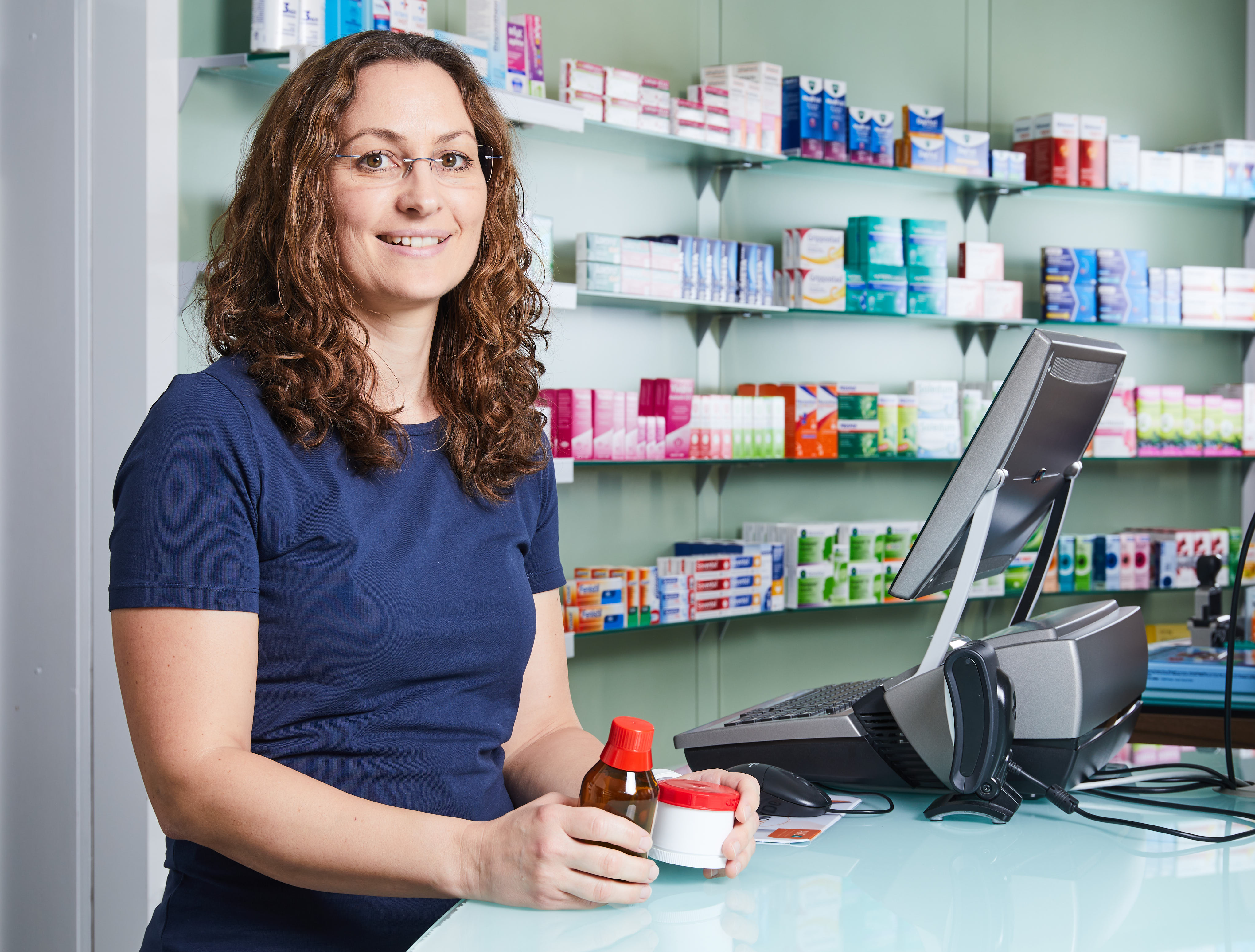 Moderne Innenansicht der Löwen-Apotheke, Apothekerin steht am Thresen mit einem Fläschchen und einem Medikament in der Hand.