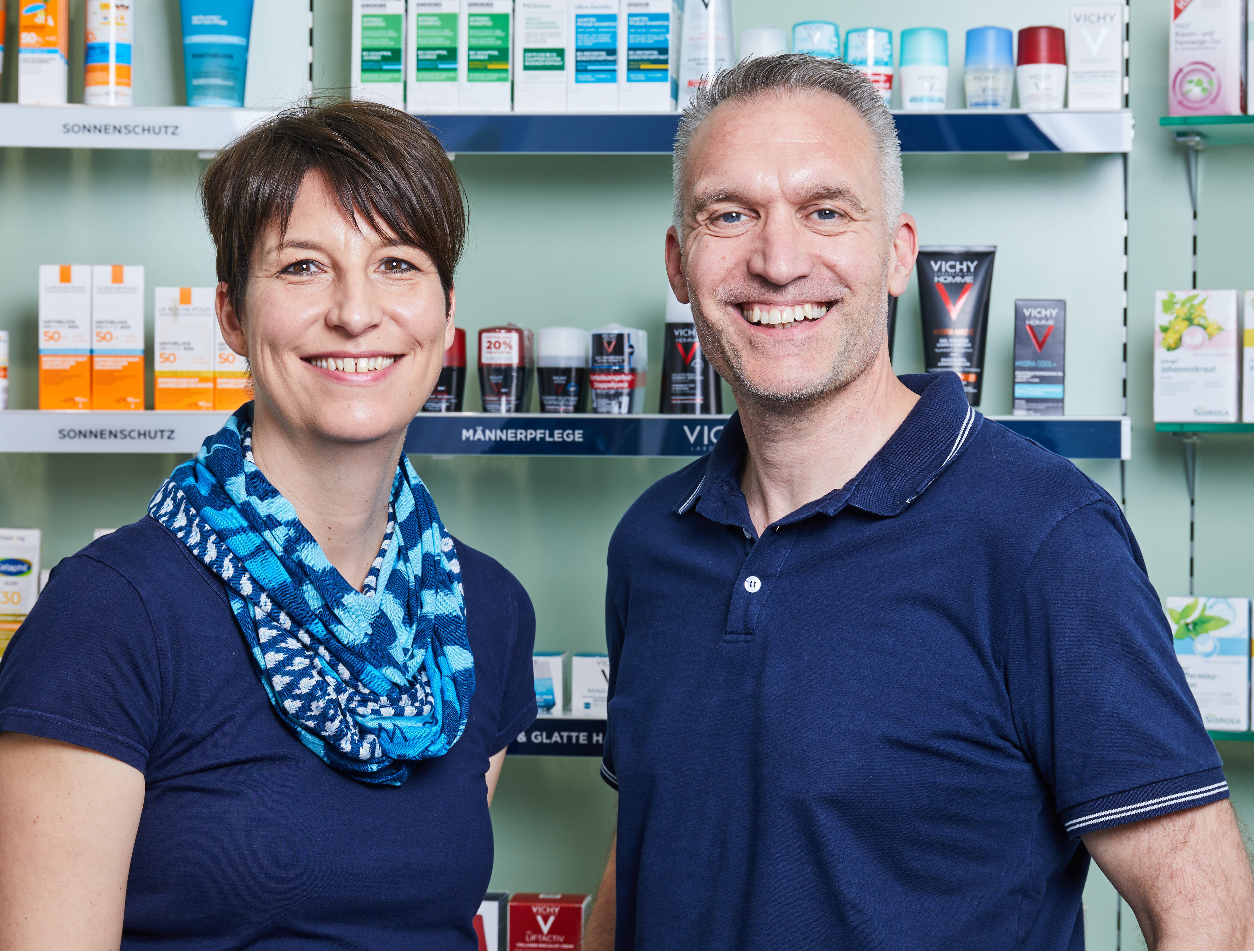 Moderne Innenansicht der Löwen-Apotheke, Inhaber und Apothekerin steht vor einem Medikamentenregal.