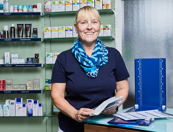 Moderne Innenansicht der Löwen-Apotheke, Apothekerin steht an Thresen mit einem Katalog in der Hand.