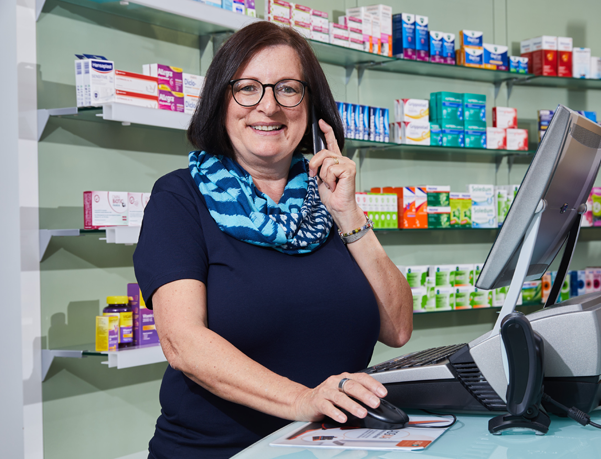 Moderne Innenansicht der Löwen-Apotheke, Apothekerin steht am PC und telefoniert.